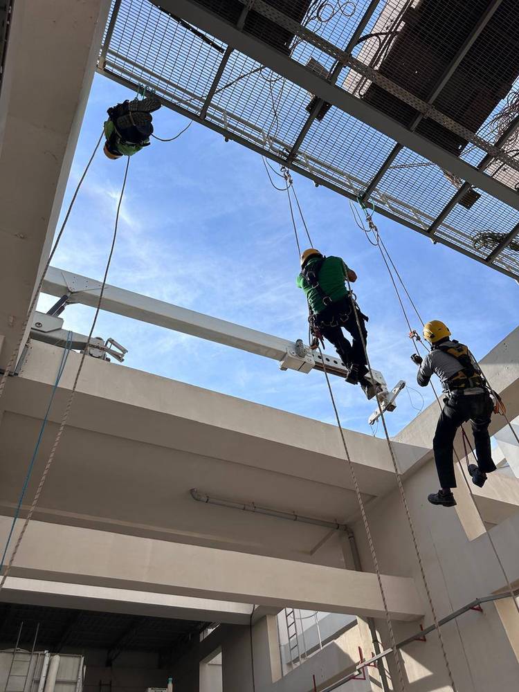 Three rope access technicians working on ropes beneath a skylight during a live job